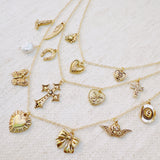 Multi-layered gold necklace featuring an eclectic mix of vintage-style charms including hearts, a cross, butterfly, bow, horseshoe, pearl, and more—creating a bold, expressive statement piece.