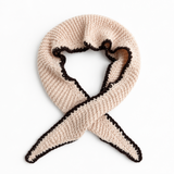 A cream-colored knit scarf with a dark brown ruffled trim, arranged in a loop with the ends crossed, on a plain white background.
