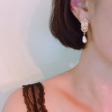 Gold oval stud earrings featuring a detailed cross design and dangling teardrop pearls—blending vintage charm with timeless elegance.