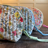 Quilted cosmetic case featuring a vintage-inspired floral print with soft padding and a structured shape, designed for storing makeup and small essentials.