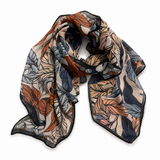 A lightweight square scarf with a botanical leaf pattern in orange, blue, gray, and black on a beige background, draped on a white studio background.