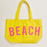Yellow tote bag with 'BEACH' written in pink on a white background