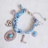 Scarf-wrapped bracelet featuring gold and sliver-tone Western-themed charms including a cowboy boot, sunburst, and lasso motifs
