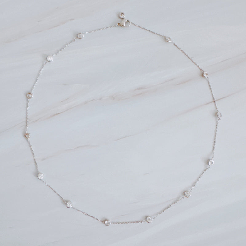 Delicate gold-tone necklace featuring twelve evenly spaced bezel-set sparkling stones along a fine chain, offering a dainty and radiant look