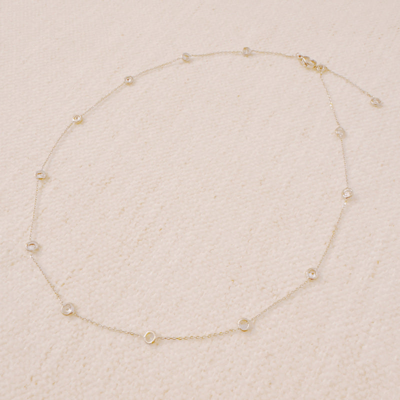Delicate gold-tone necklace featuring twelve evenly spaced bezel-set sparkling stones along a fine chain, offering a dainty and radiant look