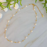 Pearl and gold necklace on a light marble surface with greenery