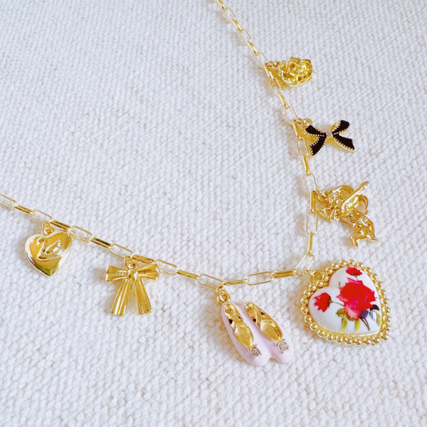  Gold-tone charm necklace featuring a dreamy mix of rose, ballet shoe, angel, and swan charms—blending grace, romance, and whimsy into a delicate statement piece.