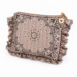 A small quilted pouch with a ruffled edge, featuring a beige bandana print with black paisley and white star details, a gold zipper, and a small gold flower charm.