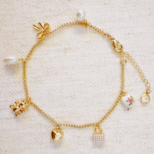 Delicate gold anklet adorned with playful charms including a bear, ribbon, heart, and pearl accents—adding a sweet and whimsical touch to your summer look.