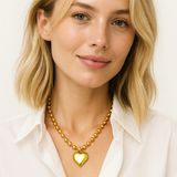 Gold-toned necklace featuring a chunky beaded chain and a bold puffed heart pendant, creating a striking statement piece with vintage flair.