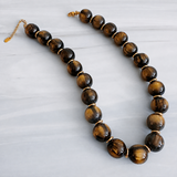 A beaded necklace made of polished tiger's eye beads with gold spacer rings and a gold clasp, displayed on a light gray marble surface.