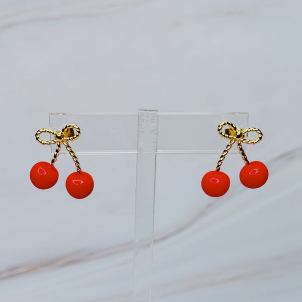 Playful gold-tone earrings featuring a bow and cherry design, adding a whimsical and charming touch to your style.