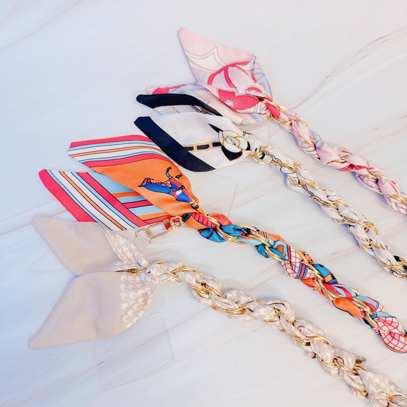 Stylish braided scarf lanyard featuring a gold-tone chain intertwined with patterned fabric, designed to securely attach to a phone while doubling as a chic fashion accessory.