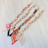 Stylish braided scarf lanyard featuring a gold-tone chain intertwined with patterned fabric, designed to securely attach to a phone while doubling as a chic fashion accessory.