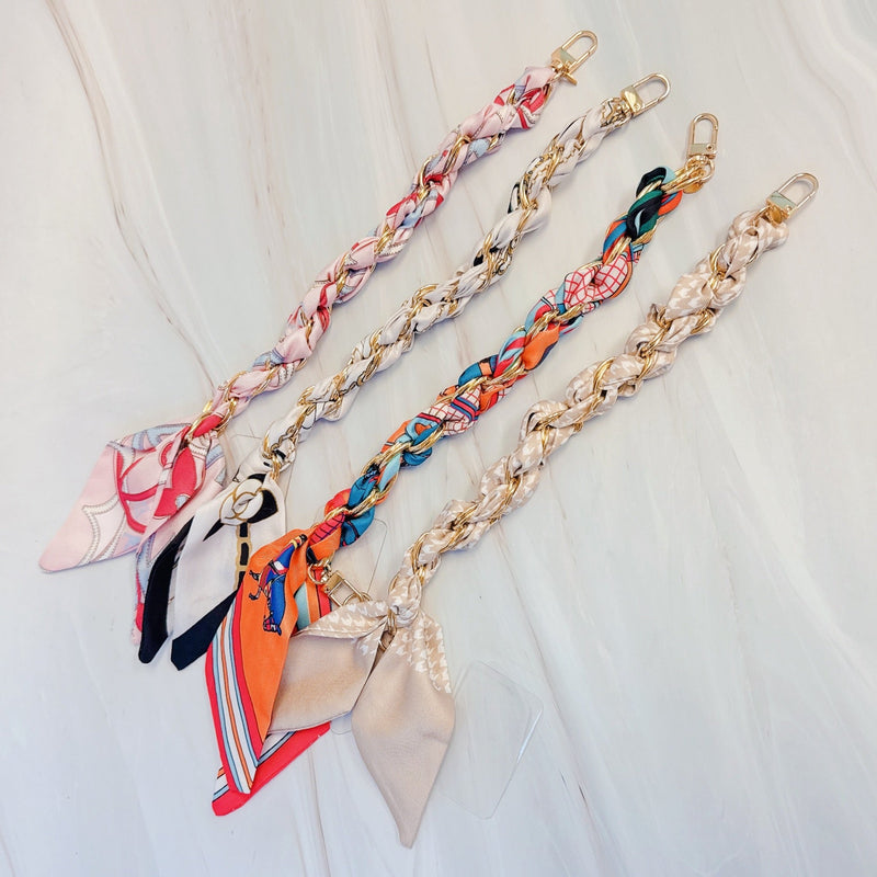 Stylish braided scarf lanyard featuring a gold-tone chain intertwined with patterned fabric, designed to securely attach to a phone while doubling as a chic fashion accessory.