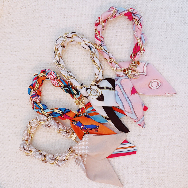 Stylish braided scarf lanyard featuring a gold-tone chain intertwined with patterned fabric, designed to securely attach to a phone while doubling as a chic fashion accessory.