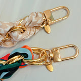 Stylish braided scarf lanyard featuring a gold-tone chain intertwined with patterned fabric, designed to securely attach to a phone while doubling as a chic fashion accessory.