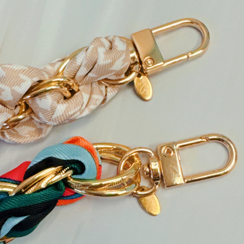 Stylish braided scarf lanyard featuring a gold-tone chain intertwined with patterned fabric, designed to securely attach to a phone while doubling as a chic fashion accessory.