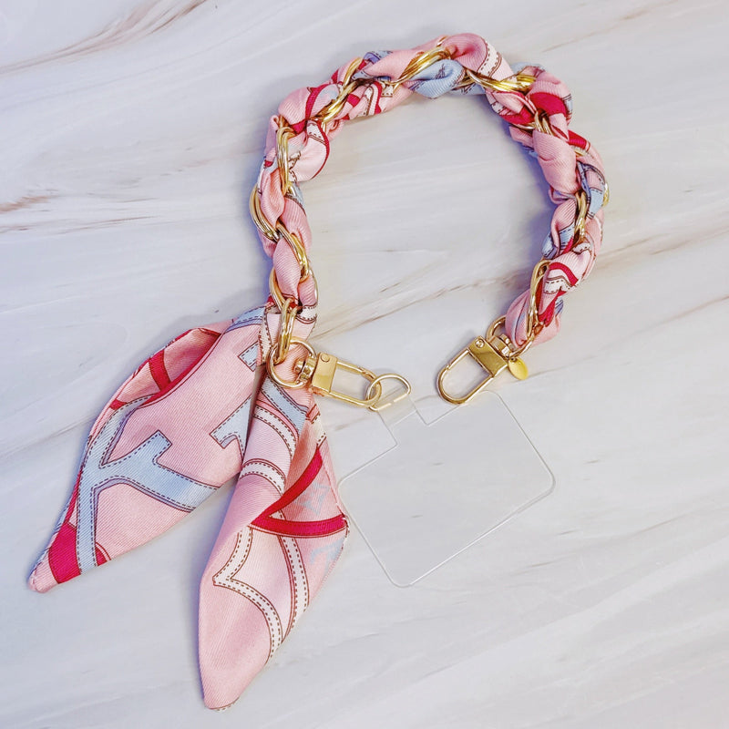 Stylish braided scarf lanyard featuring a gold-tone chain intertwined with patterned fabric, designed to securely attach to a phone while doubling as a chic fashion accessory.