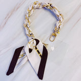Stylish braided scarf lanyard featuring a gold-tone chain intertwined with patterned fabric, designed to securely attach to a phone while doubling as a chic fashion accessory.