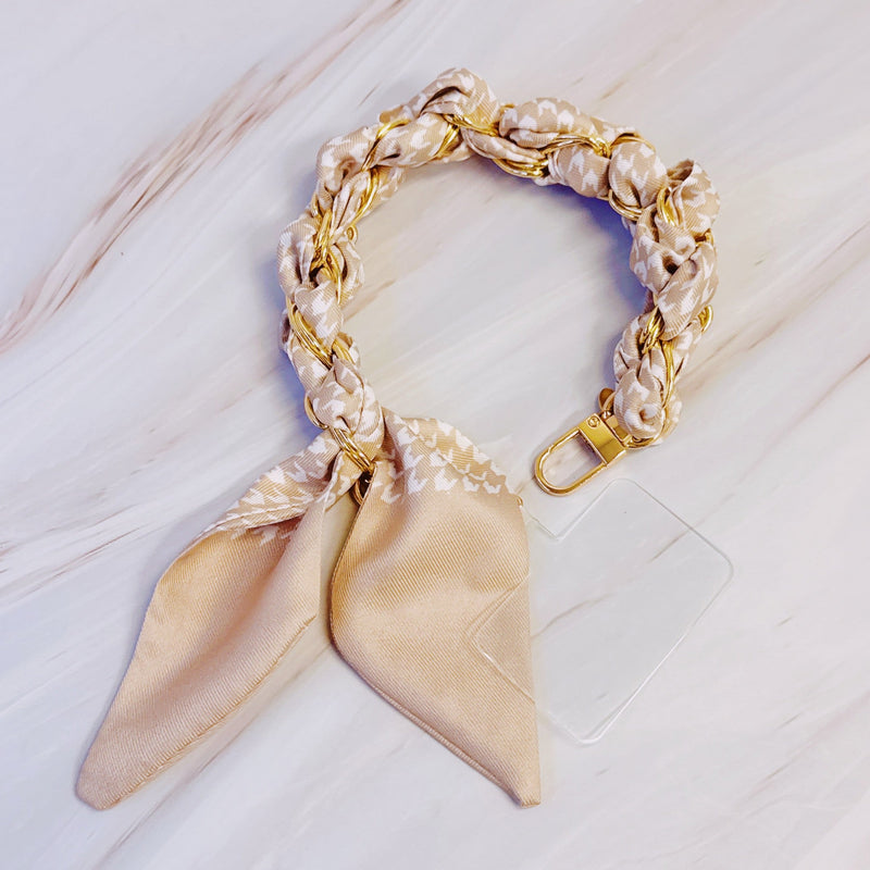 Stylish braided scarf lanyard featuring a gold-tone chain intertwined with patterned fabric, designed to securely attach to a phone while doubling as a chic fashion accessory.