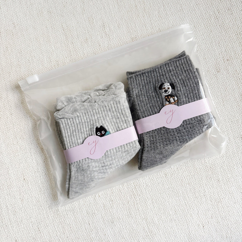 Set of two crew-length socks featuring playful cat and dog designs on a soft fabric. Each pair showcases a different animal-themed design with charming expressions and subtle color, adding a whimsical and cozy touch to everyday outfits.