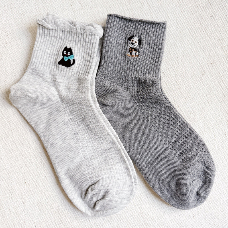Set of two crew-length socks featuring playful cat and dog designs on a soft fabric. Each pair showcases a different animal-themed design with charming expressions and subtle color, adding a whimsical and cozy touch to everyday outfits.