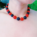 Necklace with red and black beads on a person's neck against a green leafy background