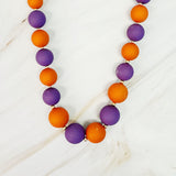 Necklace with purple and orange beads on a white wooden surface