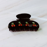 A set of two hair claws featuring a row of vibrant red cherry designs, adding a playful and fruity touch to any hairstyle.
