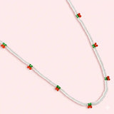 Necklace with red and green bead accents on a pink background