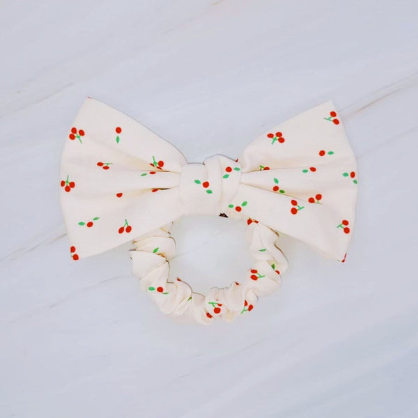 Playful hair scrunchie featuring a charming red cherry print and an attached bow tie, perfect for adding a sweet and fruity flair to ponytails or buns.