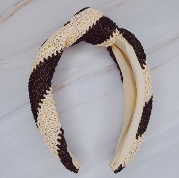 Knotted headband with bold black stripes on a beige background for a chic and modern look.