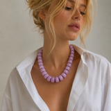 Woman wearing a white shirt and a purple necklace against a neutral background