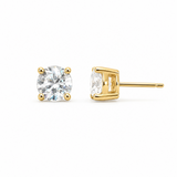 A pair of yellow gold stud earrings on a white background, showing one earring from the front with a round brilliant-cut clear gemstone and the other from the side showing the post and bezel setting.