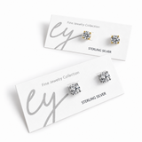 Two pairs of sterling silver stud earrings displayed on white jewelry cards. Each pair is set in a gold-tone bezel and features a square-cut clear gemstone.