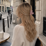 Woman with long blonde hair wearing a striped hair accessory sitting outside a cafe.