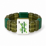 A beaded stretch bracelet featuring olive green and dark forest green translucent rectangular beads, with a central white square tile charm printed with green bamboo and the number 3.