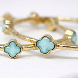 Gold bangles with turquoise clover-shaped stones on a white background