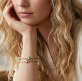Close-up of a woman wearing a gold bracelet with turquoise stones, soft focus background