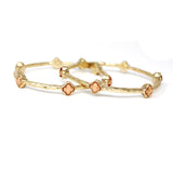 Gold bangles with clover-shaped charms on a white background