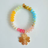 Colorful beaded stretch bracelet featuring a radiant gold-tone clover charm with an engraved initial at the center. The bracelet combines vibrant multicolored beads with a polished gold accent, creating a cheerful and personalized accessory perfect for layering or gifting.