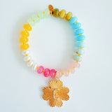 Colorful beaded stretch bracelet featuring a radiant gold-tone clover charm with an engraved initial at the center. The bracelet combines vibrant multicolored beads with a polished gold accent, creating a cheerful and personalized accessory perfect for layering or gifting.