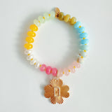 Colorful beaded stretch bracelet featuring a radiant gold-tone clover charm with an engraved initial at the center. The bracelet combines vibrant multicolored beads with a polished gold accent, creating a cheerful and personalized accessory perfect for layering or gifting.
