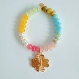 Colorful beaded stretch bracelet featuring a radiant gold-tone clover charm with an engraved initial at the center. The bracelet combines vibrant multicolored beads with a polished gold accent, creating a cheerful and personalized accessory perfect for layering or gifting.