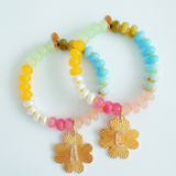 Colorful beaded stretch bracelet featuring a radiant gold-tone clover charm with an engraved initial at the center. The bracelet combines vibrant multicolored beads with a polished gold accent, creating a cheerful and personalized accessory perfect for layering or gifting.