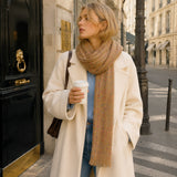 Woman in a coat and scarf holding a coffee cup on a city street.