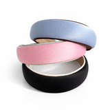 A softly padded wide headband in a solid hue, finished with a distinct contrast border trim along the edges, offering a chic and polished look for everyday wear.