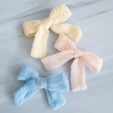 A cozy knit bow hair clip set featuring pastel-colored bows in soft shades of blue, pink, cream. Each bow is made from a textured knitted fabric, adding a charming and delicate touch to any hairstyle. Perfect for everyday wear or as a sweet accessory accent