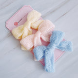 A cozy knit bow hair clip set featuring pastel-colored bows in soft shades of blue, pink, cream. Each bow is made from a textured knitted fabric, adding a charming and delicate touch to any hairstyle. Perfect for everyday wear or as a sweet accessory accent